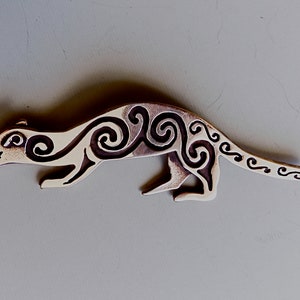 May include: A silver-coloured brooch in the shape of a stylised weasel or ferret with intricate Celtic knotwork designs.