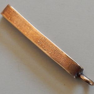 Cast bronze bar to slide onto a belt with a suspension loop at the bottom.  Back view - engraved with Master Ark, copyright 2017, Guse.