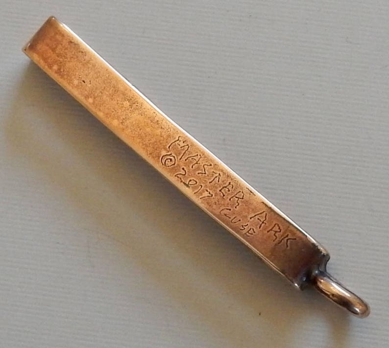 Cast bronze bar to slide onto a belt with a suspension loop at the bottom.  Back view - engraved with Master Ark, copyright 2017, Guse.