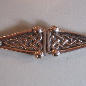 May include: A silver-toned metal clasp with a Celtic knot design. The clasp is made of two pieces that fit together.