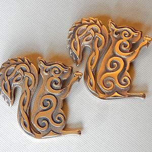 May include: Two silver-toned metal squirrel figurines with intricate Celtic knotwork designs. The squirrels are facing to the right and have their tails curled up behind them.