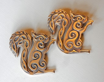 May include: Two silver-toned metal squirrel figurines with intricate Celtic knotwork designs. The squirrels are facing to the right and have their tails curled up behind them.