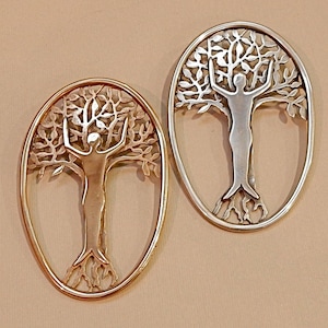May include: Two oval-shaped metal pendants, one gold and one silver, feature a tree of life design with a person standing in the center of the tree. The tree has branches and leaves, and the person has outstretched arms.