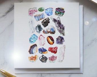 May include: A white greeting card featuring a watercolor illustration of various colorful gemstones. The gemstones include amethyst, quartz, agate, and other crystals in shades of pink, blue, green, and brown. The card is on a white background.