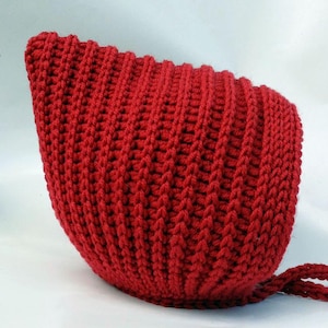 Könnte beinhalten: Eine leuchtend rote, handgestrickte Mütze mit Rippenstruktur. Die Mütze hat eine runde Form und einen Kordelverschluss. Dieser gemütliche, handgefertigte Hut ist perfekt für Babys und Kleinkinder.