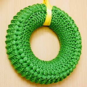 May include: A green knitted wreath with a yellow ribbon hanging from the top.