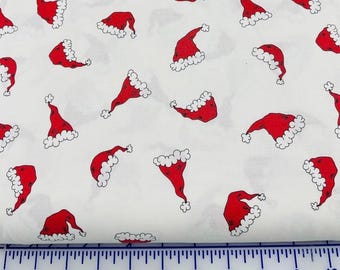 May include: White fabric with a repeating pattern of red Santa hats with white trim. The hats are outlined in black. The fabric is suitable for holiday-themed crafts and sewing projects.