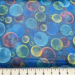May include: Fabric with a repeating pattern of overlapping, translucent bubbles in shades of blue, yellow, orange, and red against a dark blue background. A ruler is at the bottom of the image.