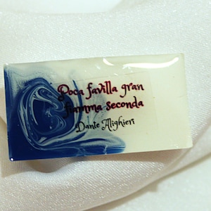 May include: A white rectangular resin paperweight with blue marbling. The paperweight has a quote in cursive script: "Poca favilla gran fiamma seconda" by Dante Alighieri.