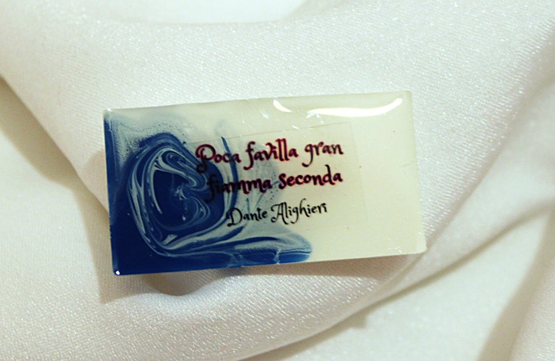 May include: A white rectangular resin paperweight with blue marbling. The paperweight has a quote in cursive script: "Poca favilla gran fiamma seconda" by Dante Alighieri.