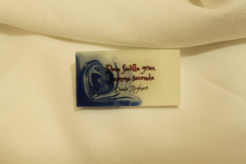 May include: A white rectangular soap bar with blue marbling. The soap has the text "Poca favilla gran fiamma seconda" and "Dante Alighieri" printed on it.