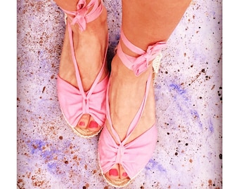May include: A pair of pink espadrille sandals with a bow detail on the straps. The sandals are worn on a person's feet and the toes are painted pink.
