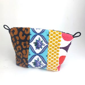Könnte beinhalten: Eine Kosmetiktasche im Patchwork-Stil mit einer Vielzahl von Mustern. Die Tasche hat einen Leoparden-, Blumen-, Waben- und Tupfen-Design. Die Tasche hat schwarze Schlaufen auf jeder Seite.