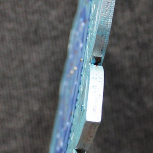 May include: A blue and silver metal snowflake ornament with a detailed design. The snowflake is made of multiple pieces that are joined together.