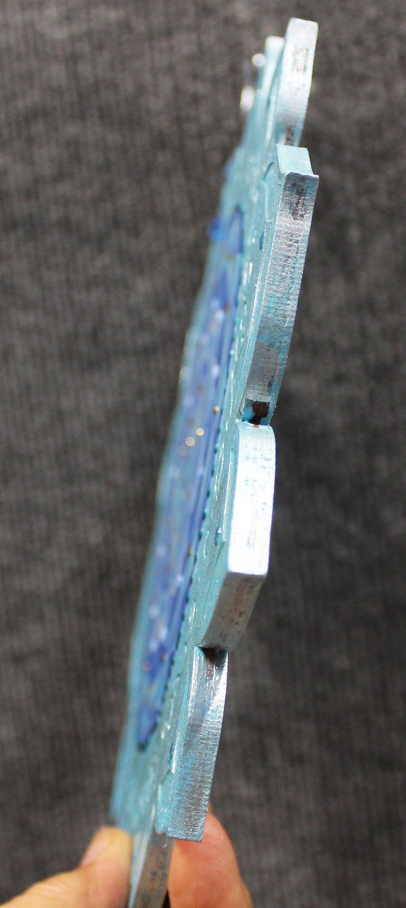 May include: A blue and silver metal snowflake ornament with a detailed design. The snowflake is made of multiple pieces that are joined together.