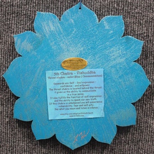 May include: A blue wooden lotus flower with a gold label that reads "5th Chakra - Vishuddha Throat chakra - color Blue (Communication)". The label also includes keywords and descriptions about the chakra.