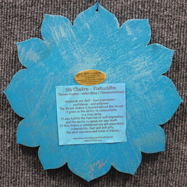 May include: A blue wooden lotus flower with a gold label that reads "5th Chakra - Vishuddha Throat chakra - color Blue (Communication)". The label also includes keywords and descriptions about the chakra.