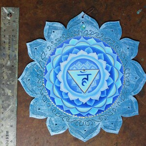 May include: A blue and white mandala with a gold trim and a blue triangle with the Sanskrit symbol "Ham" in the center. The mandala is painted on a wooden surface and has a distressed look.