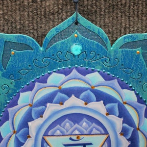 May include: A blue and white mandala with a turquoise border and gold accents. The center of the mandala features a blue and white lotus flower with a gold symbol in the center.