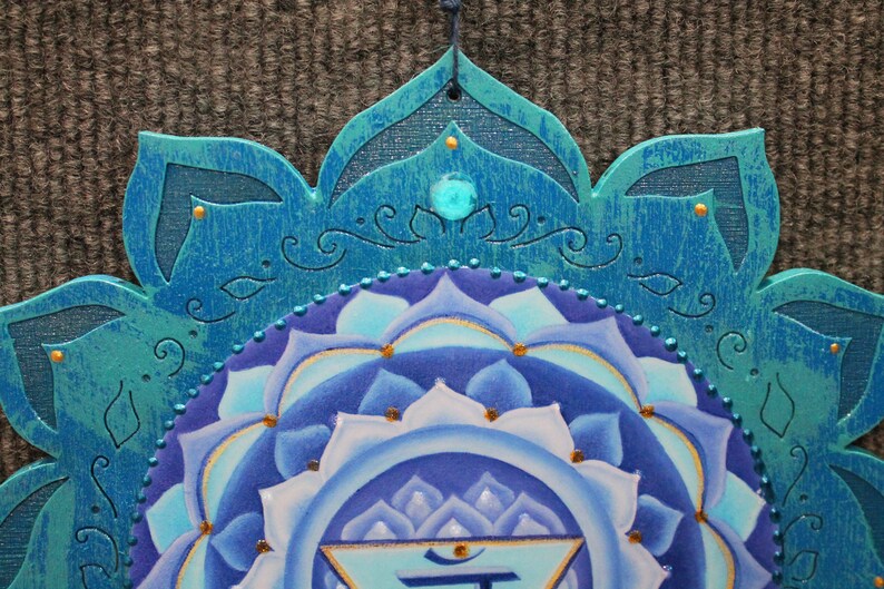 May include: A blue and white mandala with a turquoise border and gold accents. The center of the mandala features a blue and white lotus flower with a gold symbol in the center.
