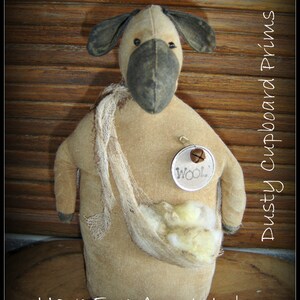 May include: A tan sheep stump doll with a dark grey face and ears, and a cream-coloured body. The doll has a burlap sack filled with wool and a tag that says "WOOL". The text "Have Ewe Any Wool~ Sheep stump Doll" is at the bottom.