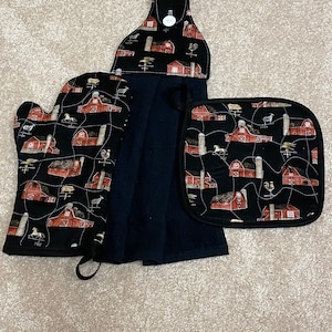 Peut inclure: Un ensemble de trois accessoires de cuisine avec un motif de grange rouge et d'animaux de ferme. L'ensemble comprend un dessous de plat, un gant de cuisine et une serviette de cuisine suspendue.