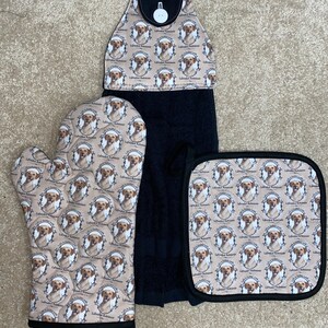 Könnte beinhalten: Ein Küchenset mit einem Labrador Retriever-Motiv. Das Set umfasst ein schwarzes Handtuch, einen Ofenhandschuh und einen Topflappen. Der gemusterte Stoff hat einen beigefarbenen Hintergrund mit sich wiederholenden Bildern eines Labrador Retrievers.