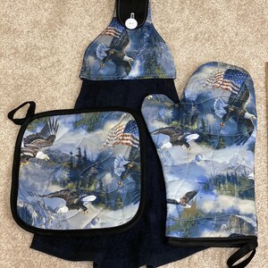 Könnte beinhalten: Ein Set aus drei Küchenaccessoires mit einem patriotischen Adler- und US-Flaggen-Design. Das Set beinhaltet einen Topflappen, einen Ofenhandschuh und ein Geschirrtuch mit einer Aufhängeschlaufe.