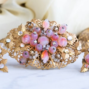 May include: A vintage gold-tone brooch and earrings set with pink and clear glass stones. The jewellery features a delicate floral design with intricate details.