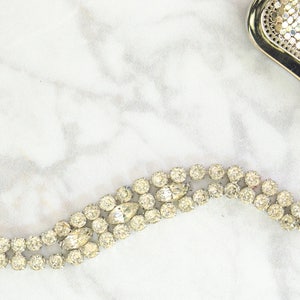May include: A vintage rhinestone bracelet with a silver chain and clasp, and a gold mesh clutch with a rhinestone clasp. The jewelry is displayed on a white marble surface.
