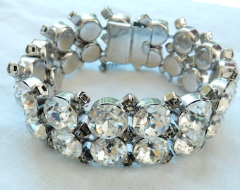 May include: A silver bracelet with a row of large clear rhinestones and a smaller row of clear rhinestones. The bracelet has a silver clasp.