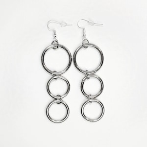 May include: Silver hoop earrings with four interconnected circles hanging from the hook.