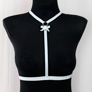 May include: White ribbon harness with a small bow and a metal ring. The harness is worn on a black mannequin.