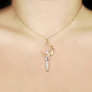 May include: A gold necklace with a crescent moon pendant featuring a small pearl and a pink gemstone. The pendant is attached to a delicate gold chain.