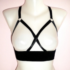 May include: Black lingerie harness with adjustable straps and a wide band. The harness has two metal rings on the straps.