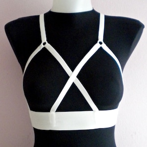 May include: White lingerie harness with adjustable straps and a wide band across the chest. The harness has two metal rings on the straps.