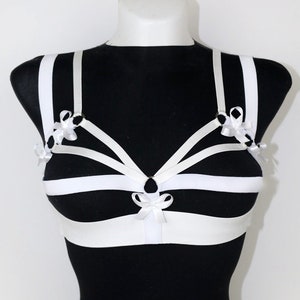 May include: White lingerie harness with multiple straps and bows. The harness is made of white elastic and has a delicate, feminine design.