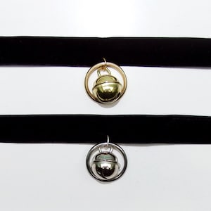 May include: Two black velvet choker necklaces with a gold and silver bell charm. The charms are round and have a raised design.