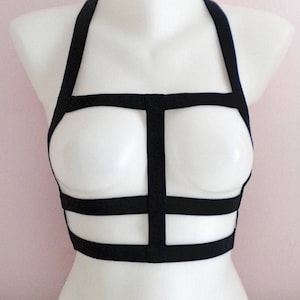 May include: Black lingerie harness with a cage design. The harness has adjustable straps and a hook closure at the back.