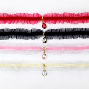 May include: Four delicate choker necklaces with a ruffled lace design and a dangling crystal pendant. The chokers are in red, black, pink, and white.