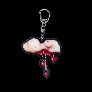 May include: A red, white and blue keychain featuring a graphic of a woman's torso with three red hearts hanging from chains. The keychain is made of acrylic and has a silver metal ring.