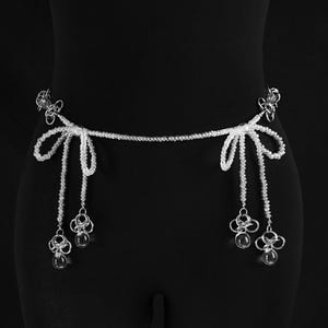 May include: A silver beaded belt with two dangling charms. The charms are made of silver and have a flower-like design. The belt is tied in a bow at the front.