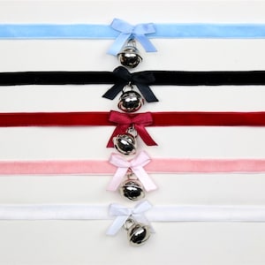May include: Five velvet ribbon chokers with silver bells and bows. The chokers are in the colours light blue, black, red, pink, and white.