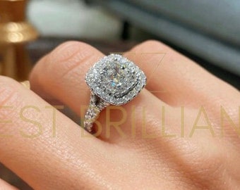 May include: A diamond engagement ring with a square halo design. The ring features a large, central diamond surrounded by smaller diamonds, set on a delicate band. The ring is shown on a person's finger.