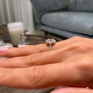 May include: A diamond engagement ring with a halo setting. The ring features a large, oval-cut diamond surrounded by smaller diamonds. The band is also encrusted with diamonds, creating a sparkling effect.