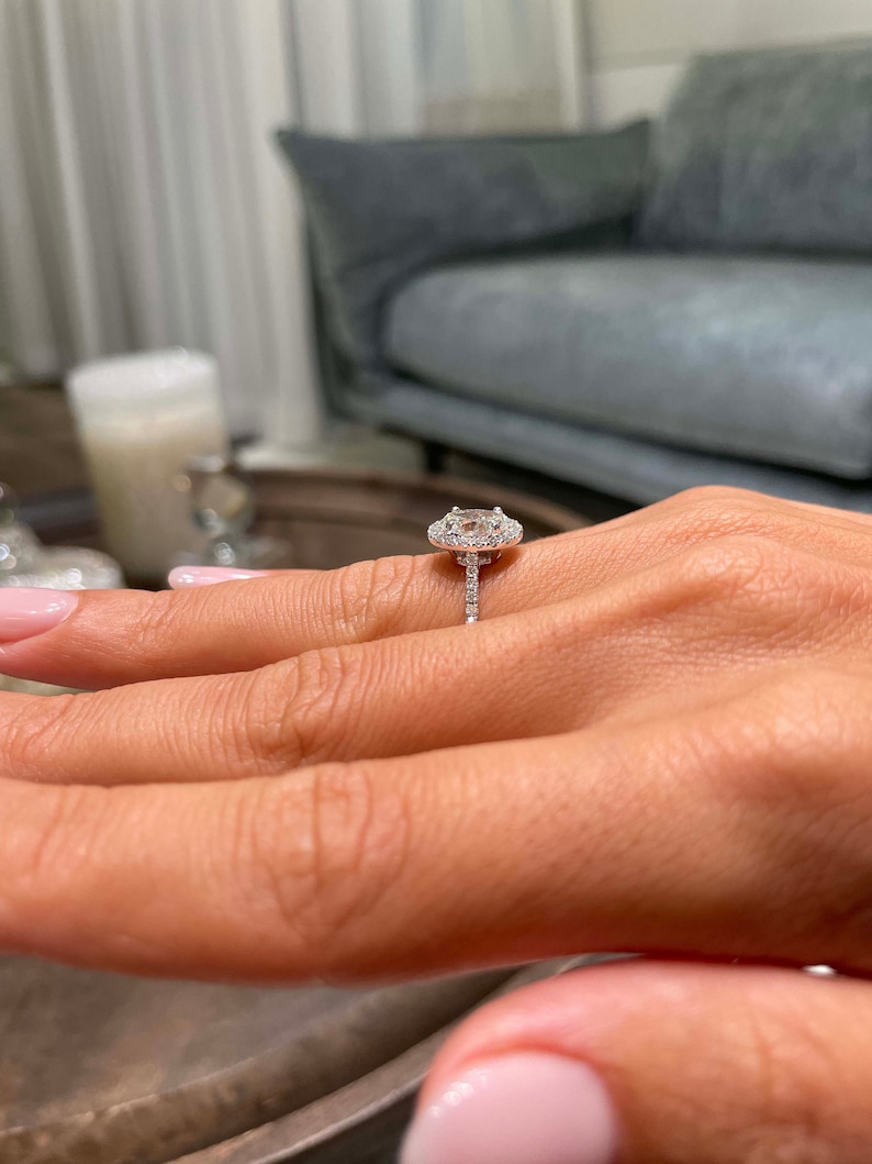 May include: A diamond engagement ring with a halo setting. The ring features a large, oval-cut diamond surrounded by smaller diamonds. The band is also encrusted with diamonds, creating a sparkling effect.