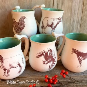 May include: Five ceramic mugs with a teal glaze and white interior. Each mug features a different farm animal illustration in brown ink: a pig, a goat, a horse, a sheep, and a chicken. The mugs have a rounded shape and a handle.
