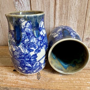 May include: Two ceramic vases with a blue and white floral pattern. One vase is upright, the other is on its side. The vases have a glossy finish and a dark blue rim. The background is a wooden surface.