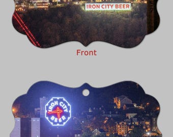 May include: Ornament featuring a nighttime cityscape with the text "IRON CITY BEER" illuminated. The front shows a crescent moon and city lights. The back displays a neon sign with the words "IRON CITY BEER".