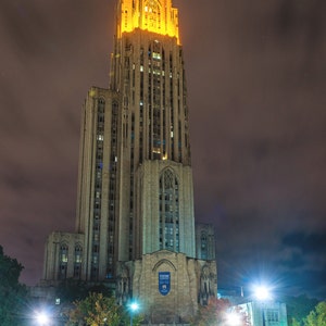 May include: A tall, illuminated building with a gothic architectural style. The building is lit up in a warm yellow light, and the sky is dark. The building has a large, arched entrance with double doors. The text "OCTOBER 8, 2016 PITT 37 - GEORGIA TECH 34" is visible at the bottom of the image.
